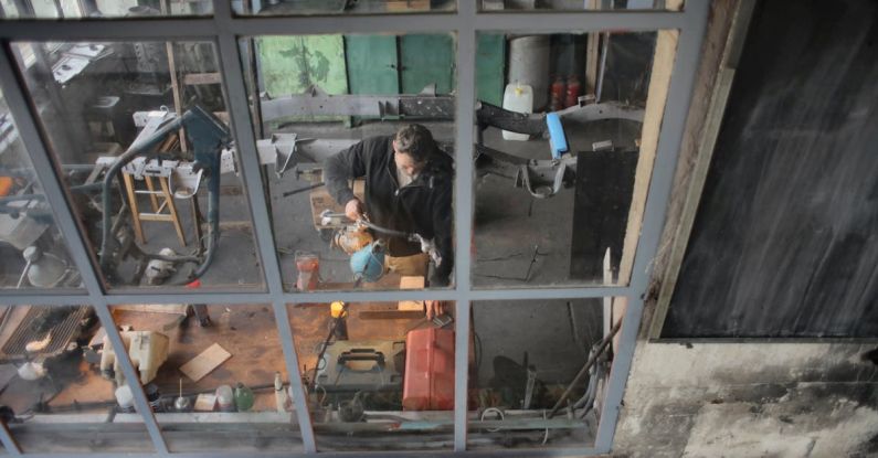Crafting Station - Through window view of male worker in casual uniform standing near workbench and working with instruments in grungy workshop