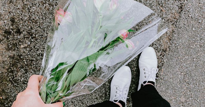 Gift - Top view of anonymous person in casual clothes and white sneakers holding bouquet of flowers and standing on asphalt
